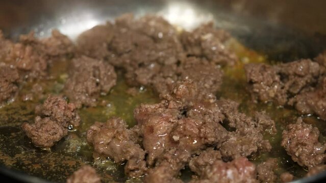 Ground beef cooking in a frying pan with fat bubbling. Slow motion rotating hamburger cooking.