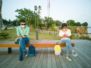 Woman and man in social distancing sitting on bench in park