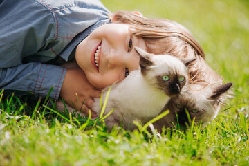 Kid plays in the summer outdoors. Сhild is friends with pet in summertime. Cute toddler is playing with a kitten on grass. Boy and baby cat