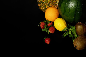 close-up of watermelon, lemon, orange, strawberry, kiwi, pineapple, dragon fruit with mint leaves on a black background