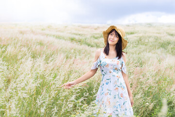 Fototapeta na wymiar The girl wearing a hat, wearing a white dress, standing in the middle of the grass with beautiful white flowers with a relaxed and happy mood.