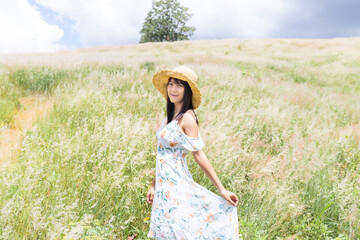 The girl wearing a hat, wearing a white dress, standing in the middle of the grass with beautiful white flowers with a relaxed and happy mood.