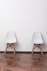 two white chairs on wooden floor in a room with white wall.