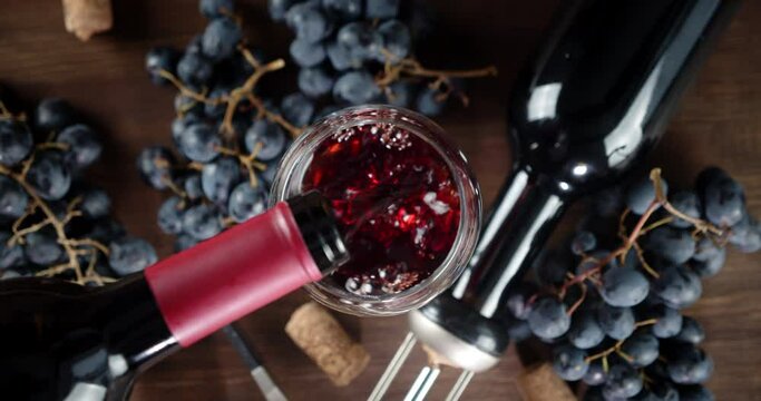 Glass on the table poured red wine from bottle.
