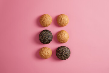 Six small soft baked burger buns sprinkled with sesame. Making hamburger or sandwich. Pink background, flat lay. Two black brioches made of cuttlefish ink. Fast food concept. Bakery products