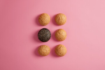 Fresh burger buns with sesame seeds arranged in two rows on rosy background. Preparing fast food or homemade hamburger. Food photography. Unhealthy eating or diet. Round soft brioches. Selective focus