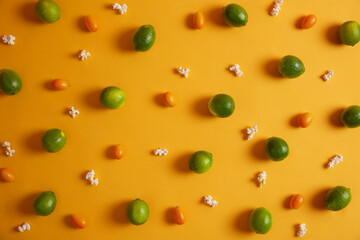 Above shot of green sour limes, cumquats and popcorn on yellow background. Summer tropical fruits. Assortment of citrus. Nobody on photo. Food and nutrition concept. Vitamins, minerals concept
