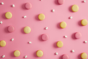 Colored round delicious macaroons and marshmallow on pink pastel background. Tasty french dessert containing much sugar. Diet, calories, confectionery concept. Homemade appetizing food. Top view