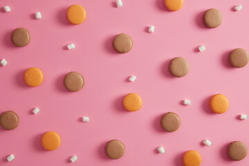 Two colored fresh french macaroons with marshmallow isolated over rosy background. Tasty dessert for real gourmands. High calories food. Cookies to satisfy your sweet tooth. Chocolate, orange flavor