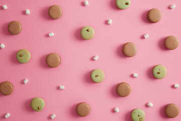 Delicious green pistachio and chocolate macaroons with marshmallow against rosy background. Sweet confectionery. Round french yummy cookies for eating. Flat lay and top view. Appetizing snack