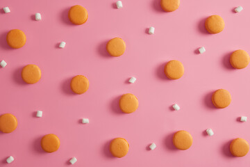 Food and bakery concept. Delicious orange round french macaroons and marshmallow over rosy studio background. Pleasant flavor. Assortment of tasty cookies. Tasty macarons. Menu dessert label