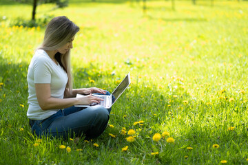 Young woman with laptop sitting on green grass