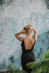 Naklejka premium Back view of a blond woman in black backless dress, blu abstract wall in the background.