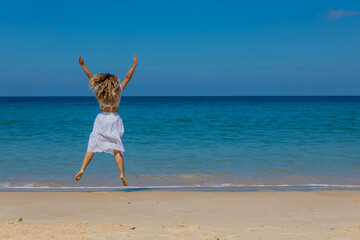 Young beautiful girl in white clothes walks along the sandy beach near the water