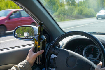 A bottle of wine in the hand of a driver traveling at high speed. Concept of unacceptable and dangerous car driving.