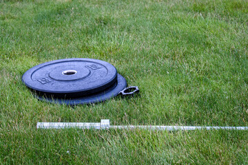 Olympic barbell with black weight plates on a green lawn, ready for an outdoor workout

