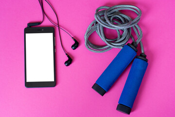 Jump rope and smartphone with headphones on pink background. Top view.