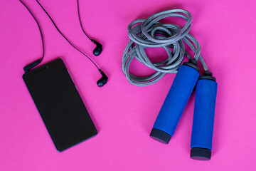 Jump rope and smartphone with headphones on pink background. Top view.