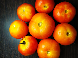 A shot from top of a group of fresh tomatoes arranged in a proper arrangement in a orange coloured bowl with good lighting method.