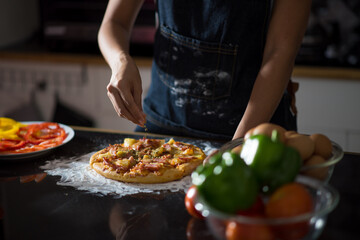 close-up of human hands in the apron knead the dough on a black wooden table, sprinkle with flour.Making dough by hands at bakery.
