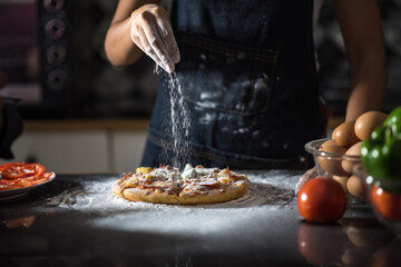 close-up of human hands in the apron knead the dough on a black wooden table, sprinkle with flour.Making dough by hands at bakery.