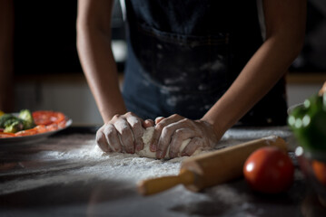 close-up of human hands in the apron knead the dough on a black wooden table, sprinkle with flour.Making dough by hands at bakery.