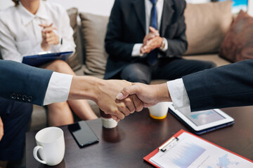 Business people shaking hands over table with financial documents after closing deal