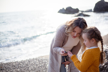 Happy family posing outdoor in the beach of the sea at spring time. woman with daughter have fun on vacation near ocean. Female parent show smth to child . Travel, love, holidays concept - lifestyle