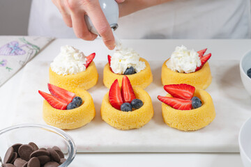 Biscuit cakes with fresh berries, chocolate, and whipped heavy cream. Fresh mini biscuit cups close up on white background, woman hands