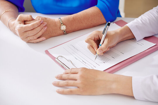 Hands Of Health Insurance Agent Talking To Senior Woman And Filling Medical Insurance Form