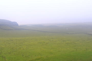 Fototapeta premium White fog cover over dandscape green grasses in flied of yorkshire dale, Malham