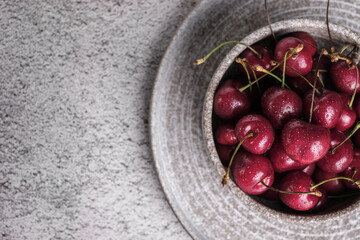 Red cherry berry  with drops of water at rustic ceramic plate at wooden background