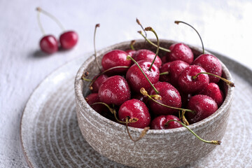 Red cherry berry  with drops of water at rustic ceramic plate at wooden background