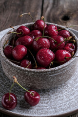 Red cherry berry  with drops of water at rustic ceramic plate at wooden background