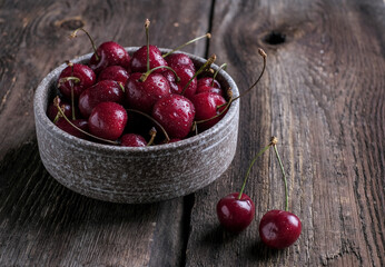 Red cherry berry  with drops of water at rustic ceramic plate at wooden background