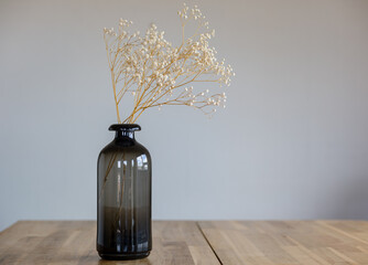 A dark glass vase with a dry flower stands on a wooden surface.