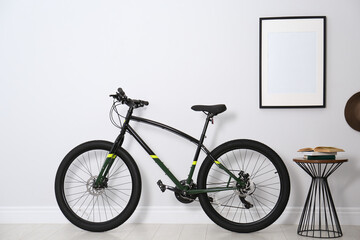 Modern black bicycle near light wall indoors