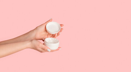 Closeup of young lady holding open jar of cream on pink background, empty space