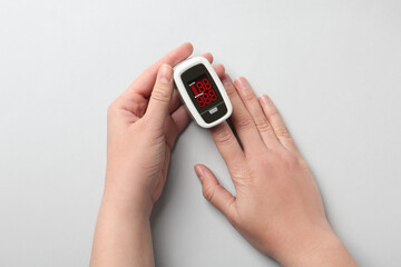 Woman using fingertip pulse oximeter on white background, top view