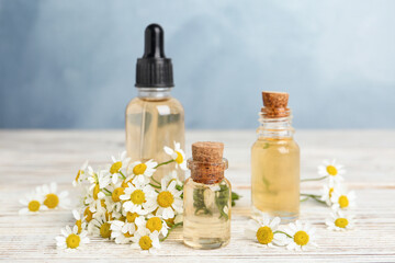 Bottles of essential oil and chamomiles on white wooden table