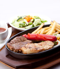 Chicken breast steak, beef steak, fried sausages, french fries, served on a hot plate, with pickles and barbecue sauce.