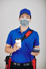 Fototapeta na wymiar Portrait of cheerful courier holding payment terminal and cup of take out coffee