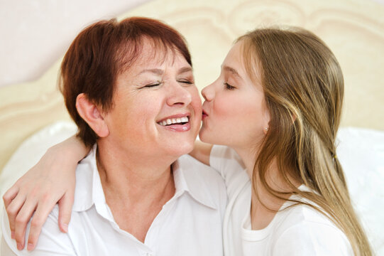 Cute little granddaughter child kissing smiling old grandmother on cheek