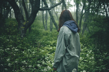 back view of a girl walking along a path through a gloomy mystical foggy forest. Trekking and outdoor concept.