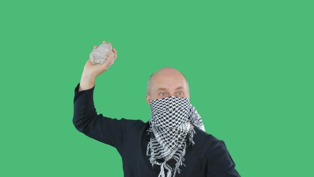 Anarchist protestor in checkered bandana swings stone on green screen chroma key background on demonstration. Bald vandal with stone on protest civil revolution. Social riots and uprisings concept