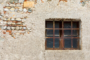 Vecchia finestra con sbarre su edificio con muro di sasso. Vecchia casa.