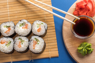 Sushi rolls set served on bamboo mat. Blue background