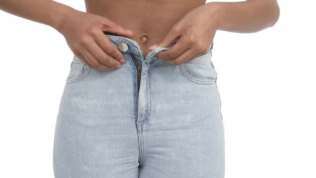 Front view of unrecognizable slim fit African woman lower body part. Zipping tight light blue skinny jeans on her body. Isolated, on white background