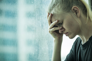 Closeup of sad crying young woman with hand on face crying by the window. Depression/Loneliness concept.