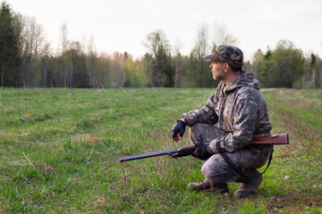 a hunter with a shotgun squats in a clearing